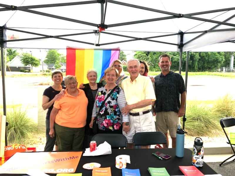 Eight people stand in a group under the PFLAG tent at a Pride nonprofit showcase in 2021.